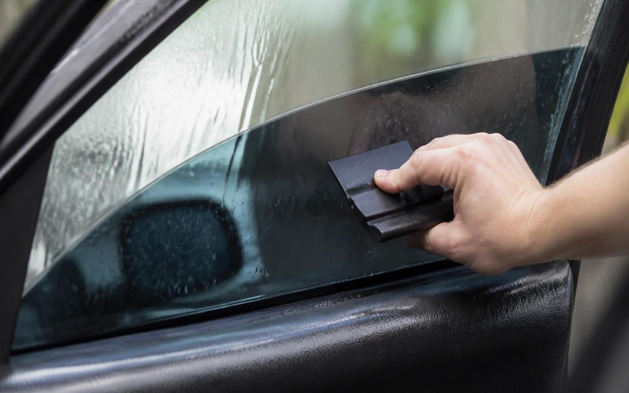 Hand pressing tint film onto a wet car side window with a squeegee during car window tinting